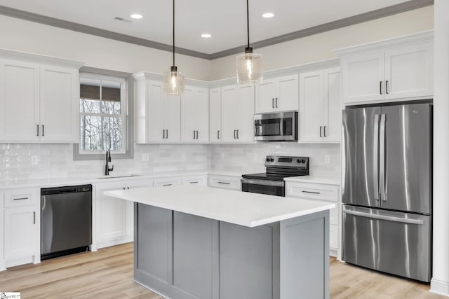 kitchen featuring crown molding, light countertops, appliances with stainless steel finishes, white cabinets, and a sink