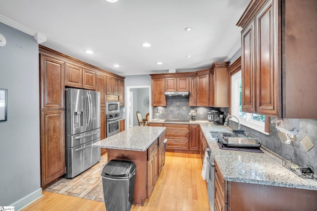 kitchen with under cabinet range hood, light stone counters, stainless steel appliances, and light wood-style floors