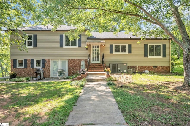 tri-level home with brick siding, cooling unit, entry steps, and a front yard