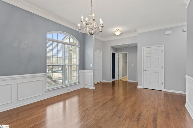 unfurnished room with a wainscoted wall, an inviting chandelier, wood finished floors, and ornamental molding