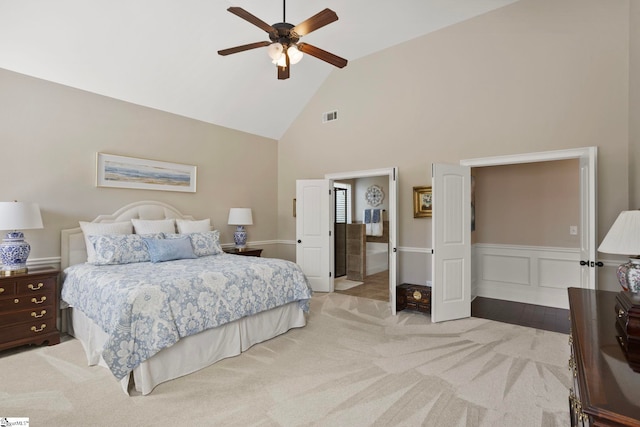 bedroom featuring a wainscoted wall, visible vents, high vaulted ceiling, a decorative wall, and light colored carpet