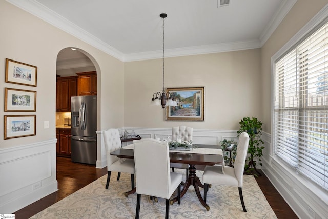 dining room with dark wood finished floors, arched walkways, wainscoting, crown molding, and a chandelier