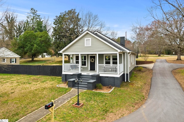 bungalow with fence, a front yard, covered porch, a chimney, and driveway