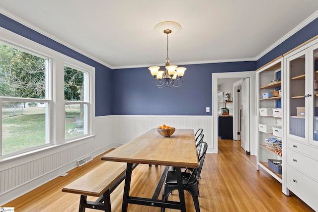 dining space with light wood-type flooring, a wainscoted wall, visible vents, and a chandelier