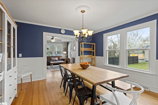 dining room with crown molding, a notable chandelier, a wainscoted wall, and light wood finished floors