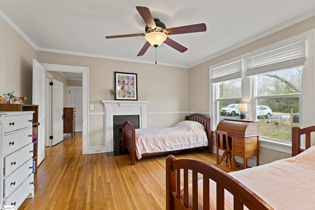 bedroom featuring a fireplace with flush hearth, light wood-style flooring, crown molding, and ceiling fan