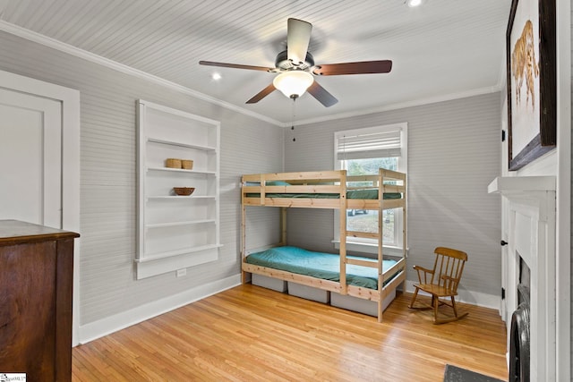 bedroom featuring baseboards, wood finished floors, a fireplace, and ornamental molding