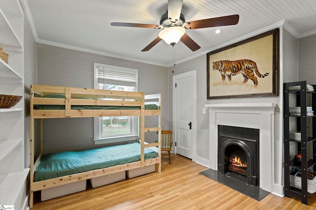 bedroom with a fireplace with flush hearth, a ceiling fan, wood finished floors, and crown molding