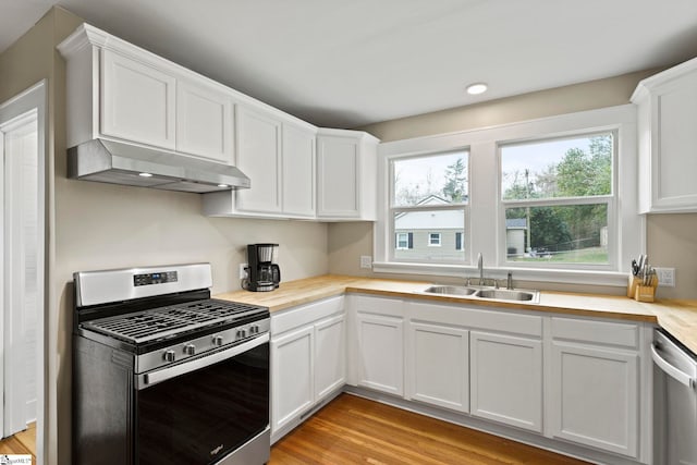 kitchen with under cabinet range hood, stainless steel appliances, white cabinets, and a sink