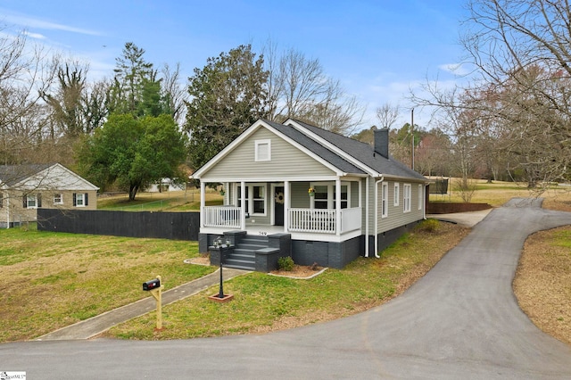 view of front of home with a front lawn, aphalt driveway, a porch, crawl space, and a chimney