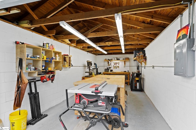 basement featuring electric panel, a workshop area, and concrete block wall