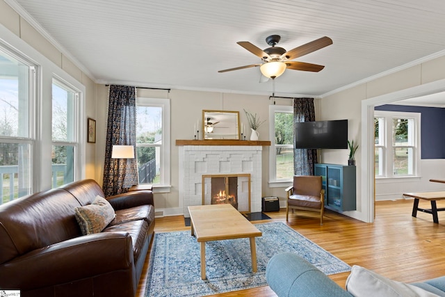 living room featuring a brick fireplace, crown molding, a wealth of natural light, wood finished floors, and a ceiling fan