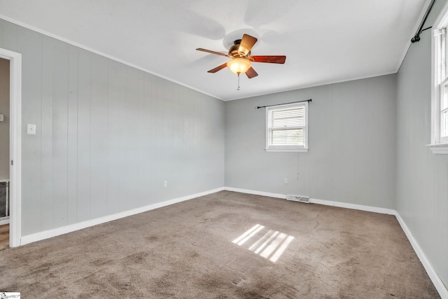 carpeted empty room with visible vents, baseboards, crown molding, and ceiling fan