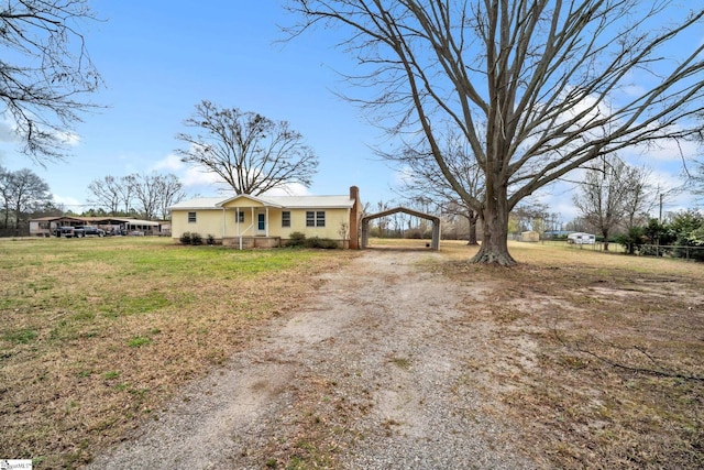 ranch-style home with a chimney, a front yard, a detached carport, and driveway