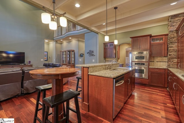 kitchen with glass insert cabinets, dark wood-type flooring, appliances with stainless steel finishes, arched walkways, and a sink