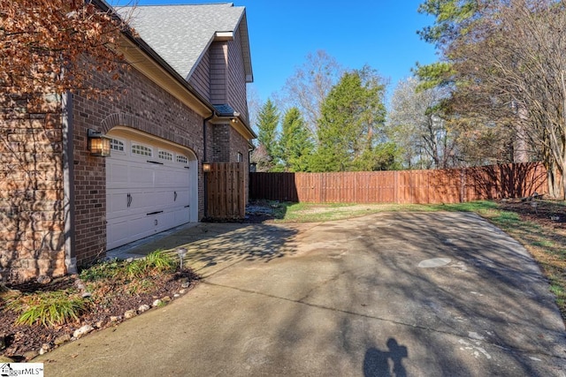 view of home's exterior with brick siding, a shingled roof, fence, a garage, and driveway