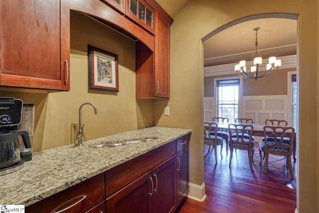 kitchen featuring light stone counters, dark wood-style flooring, a sink, glass insert cabinets, and a chandelier