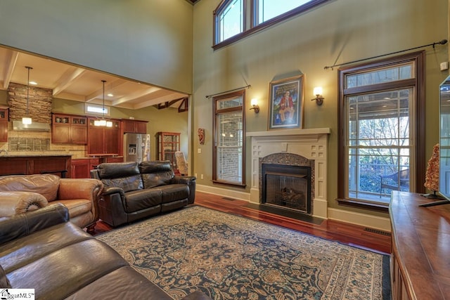 living area with visible vents, a fireplace with flush hearth, beam ceiling, wood finished floors, and baseboards