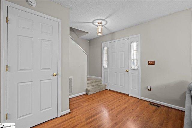 entryway featuring visible vents, baseboards, stairway, wood finished floors, and a textured ceiling