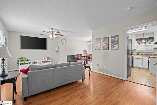 living room with a ceiling fan, light wood-type flooring, and a textured ceiling