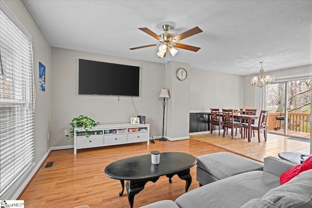 living room with ceiling fan with notable chandelier, light wood-type flooring, and a textured ceiling