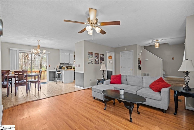 living area with stairway, visible vents, light wood-style flooring, a textured ceiling, and ceiling fan with notable chandelier