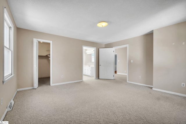 unfurnished bedroom featuring light carpet, ensuite bathroom, a closet, baseboards, and a spacious closet