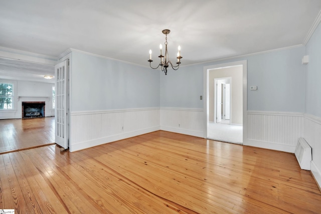 unfurnished dining area featuring light wood-type flooring, ornamental molding, wainscoting, a fireplace, and a notable chandelier