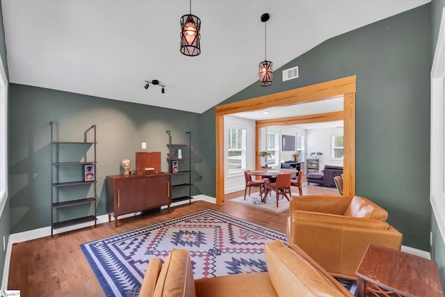 living room featuring wood finished floors, visible vents, baseboards, vaulted ceiling, and rail lighting