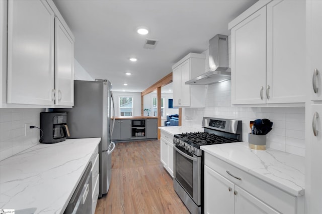 kitchen featuring visible vents, light wood-type flooring, appliances with stainless steel finishes, white cabinetry, and wall chimney exhaust hood