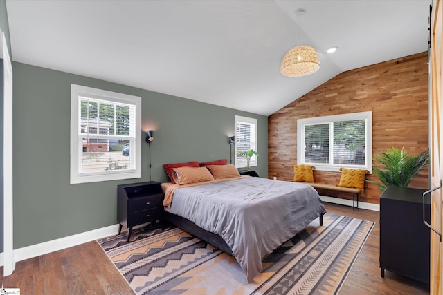 bedroom featuring wooden walls, wood finished floors, baseboards, and vaulted ceiling