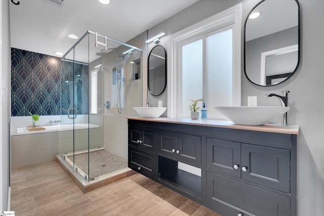 bathroom featuring double vanity, a stall shower, wood finished floors, and a sink