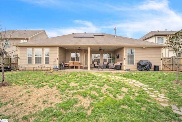 rear view of property featuring a patio, a gate, a ceiling fan, a lawn, and roof mounted solar panels