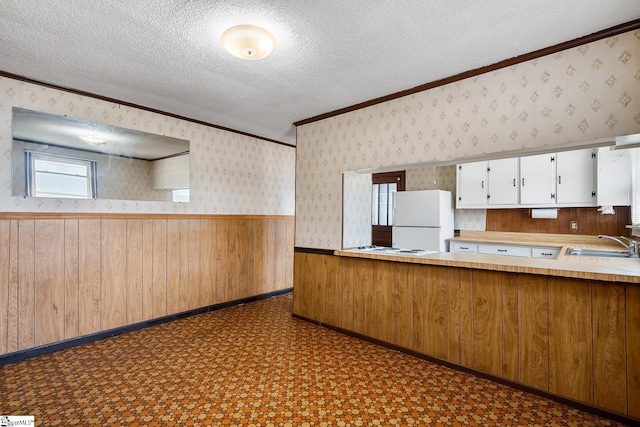 kitchen with a wainscoted wall, a sink, a textured ceiling, freestanding refrigerator, and wallpapered walls