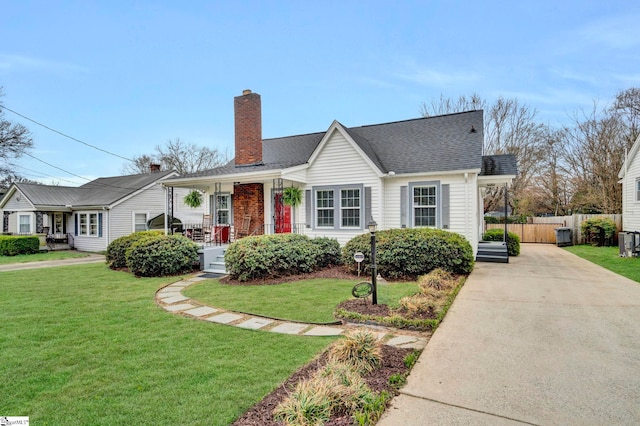 view of front of house with covered porch, a chimney, a front yard, and fence