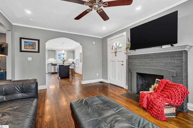 living area with crown molding, arched walkways, dark wood-style flooring, and ceiling fan