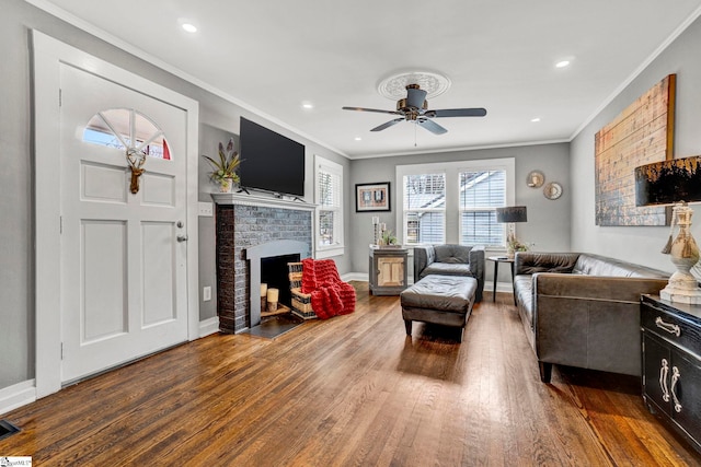 living room featuring ornamental molding, a fireplace, ceiling fan, and wood finished floors