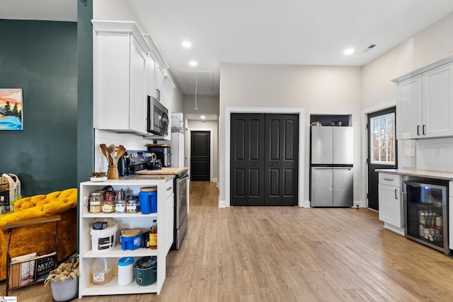 kitchen featuring light wood-style flooring, stainless steel appliances, wine cooler, white cabinets, and decorative backsplash