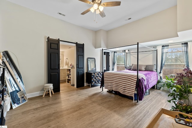 bedroom with visible vents, light wood-style flooring, baseboards, and a barn door