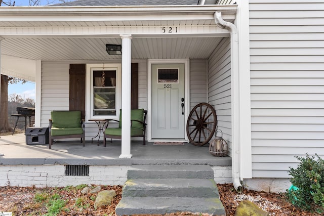 view of exterior entry with a porch and a shingled roof