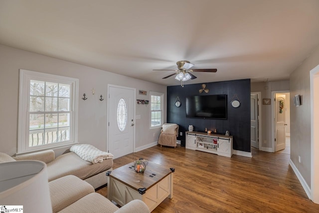 living area featuring a healthy amount of sunlight, baseboards, a ceiling fan, and wood finished floors