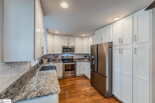 kitchen with light stone counters, dark wood-style flooring, a sink, appliances with stainless steel finishes, and white cabinetry