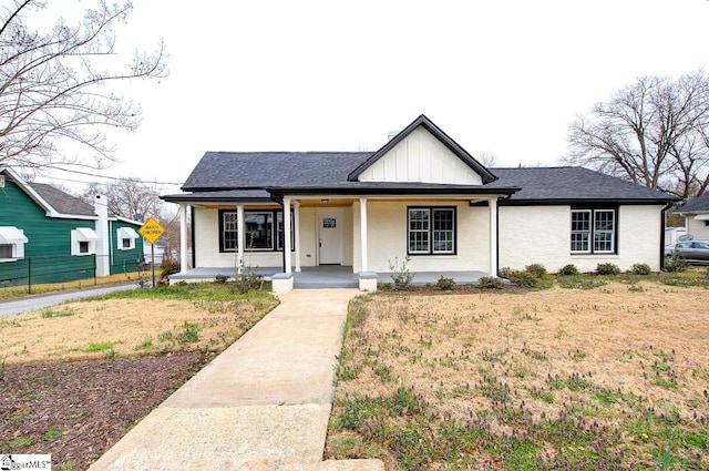 view of front of home featuring a porch, fence, board and batten siding, a shingled roof, and brick siding