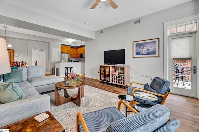 living room with baseboards, wood finished floors, visible vents, and ceiling fan