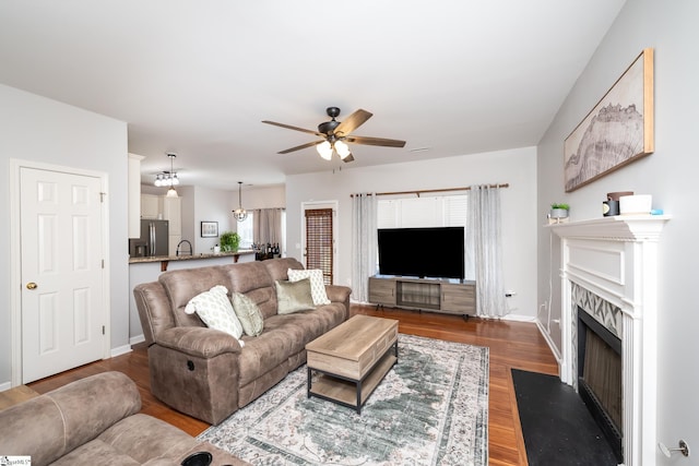 living area featuring a fireplace with flush hearth, wood finished floors, baseboards, and ceiling fan