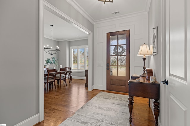 entrance foyer with visible vents, baseboards, ornamental molding, an inviting chandelier, and wood finished floors