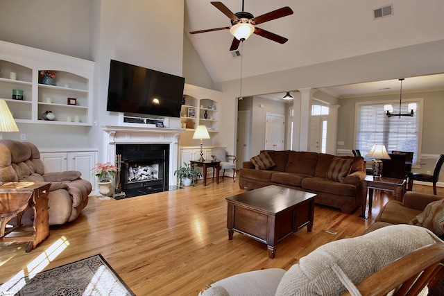 living area featuring visible vents, a fireplace with flush hearth, ceiling fan with notable chandelier, a towering ceiling, and wood finished floors