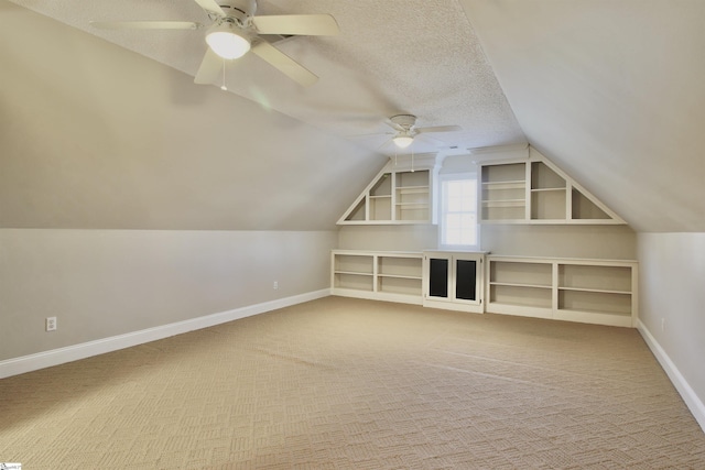 bonus room featuring lofted ceiling, a textured ceiling, carpet, baseboards, and ceiling fan