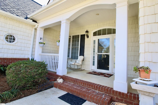 doorway to property featuring roof with shingles and a porch