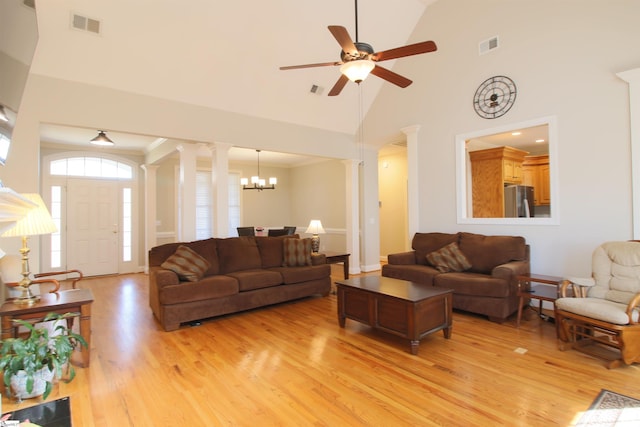 living area with visible vents, light wood-style flooring, ceiling fan with notable chandelier, high vaulted ceiling, and ornate columns